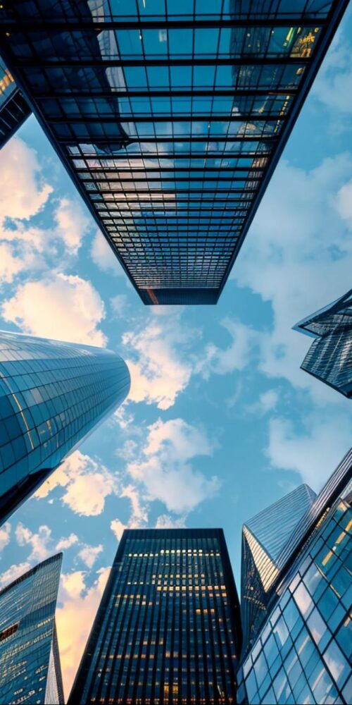 Looking up at modern glass skyscrapers against a blue sky with clouds.